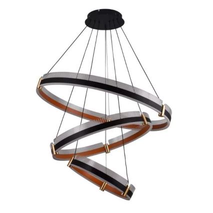 Trojitý kruhový luster visí zo stropu. Kruhy sú prepletené do špirálovitého tvaru, pričom každý je zložený z priehľadného a tmavého materiálu s kovovými prvkami.