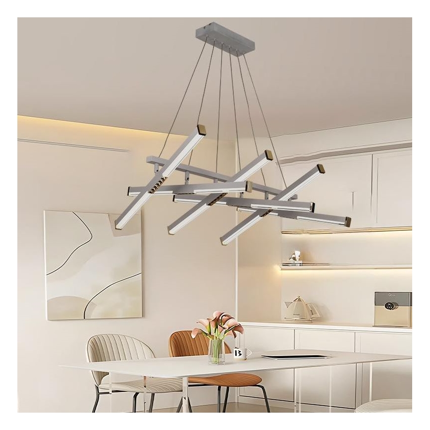 Moderná strieborná LED lustre visí nad jedálenským stolom v minimalistickej jedálni. Lustre pozostáva z viacerých rovnobežných svetelných ramien usporiadaných do asymetrického vzoru. Okolité prostredie tvorí svetlý nábytok a neutrálne steny.