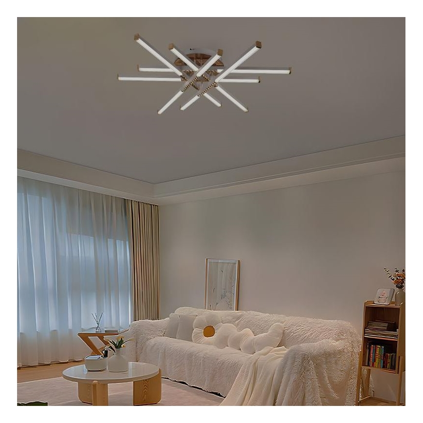 Stropné svietidlo s viacerými bielymi tyčinkovými ramenami osvetľuje obývaciu izbu. Svietidlo je pripevnené k stropu a jeho ramená sa rozprestierajú do strán. Izba obsahuje bielu sedačku, konferenčný stolík a závesy.