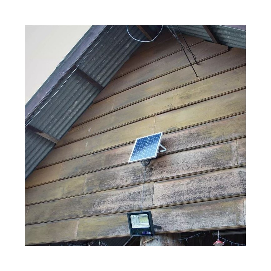 Solárny panel nabíja vonkajšie LED svetlo. Svetlo je pripevnené na drevenú stenu budovy s plechovou strechou.