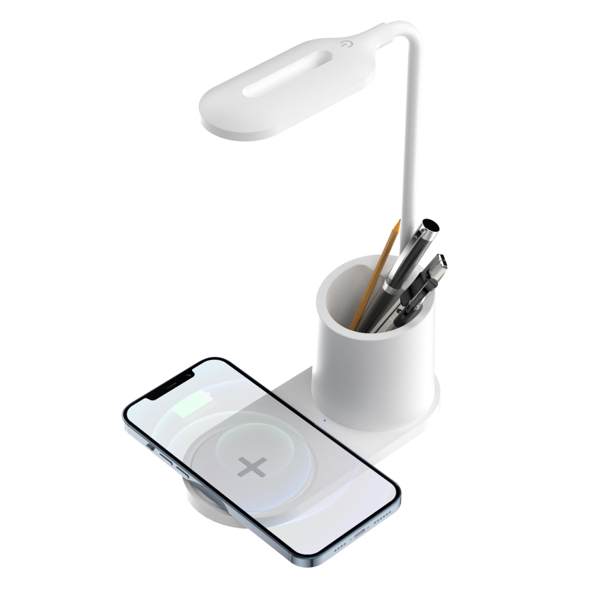 Biela stolná lampa s nabíjačkou na telefón a držiakom na perá. Telefón sa nabíja bezdrôtovo. Pero, ceruzka a ďalšie písacie potreby sú v držiaku.