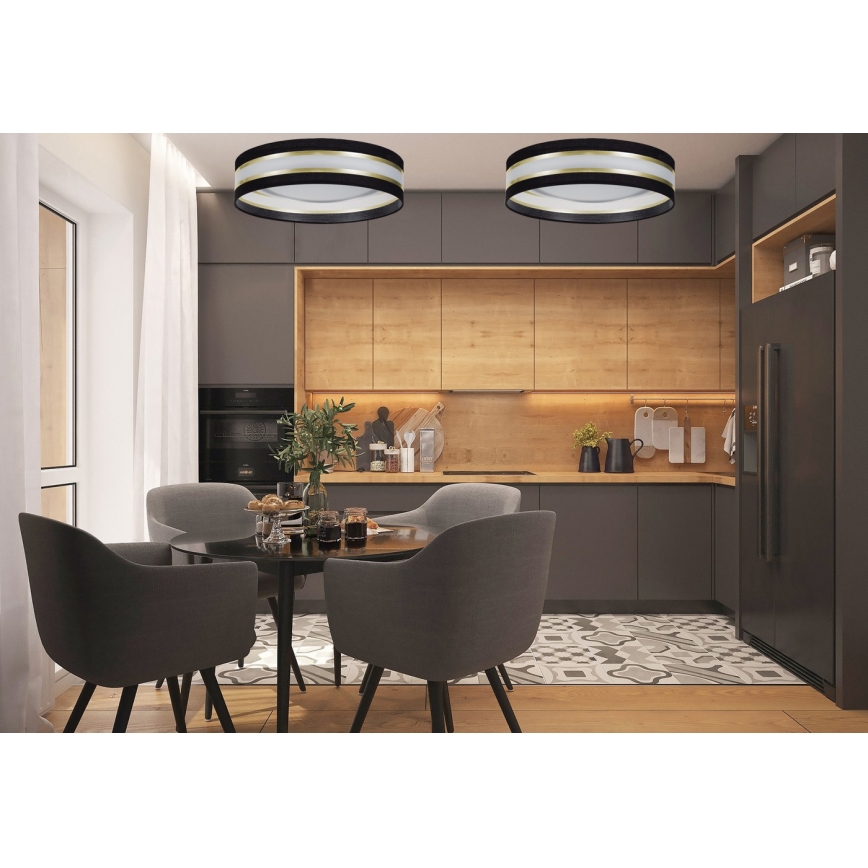 Dve stropné svietidlá s čiernym tienidlom a zlatým lemom osvetľujú jedáleň. Svietidlá sú umiestnené v kuchyni s drevenými skrinkami a tmavosivou pracovnou doskou. Stôl s tmavými stoličkami sa nachádza v strede jedálne.