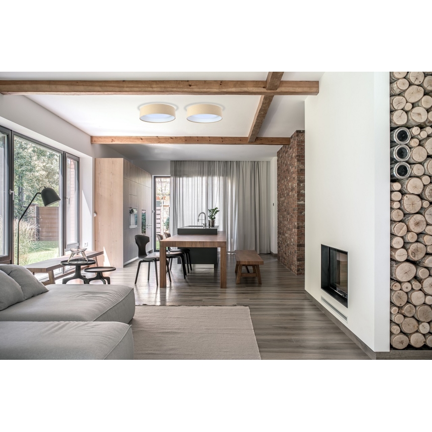 Dve stropné svietidlá svietia v obývacej izbe s jedálenským kútom a krbom. Svetlý interiér s drevenými prvkami.