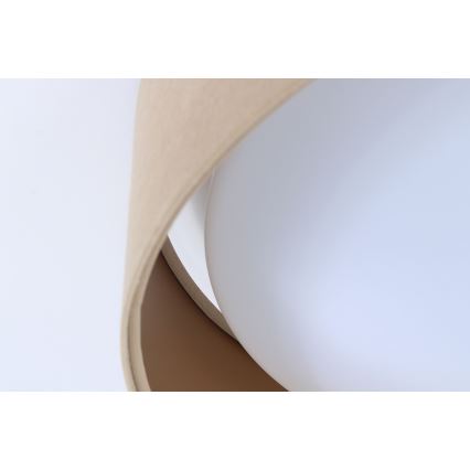 Svietidlo svieti. Je zložené z dvoch častí, svetlejšej a tmavšej béžovej, ktoré obklopujú bielu guľovú časť. Svietidlo je umiestnené na svetlom pozadí.