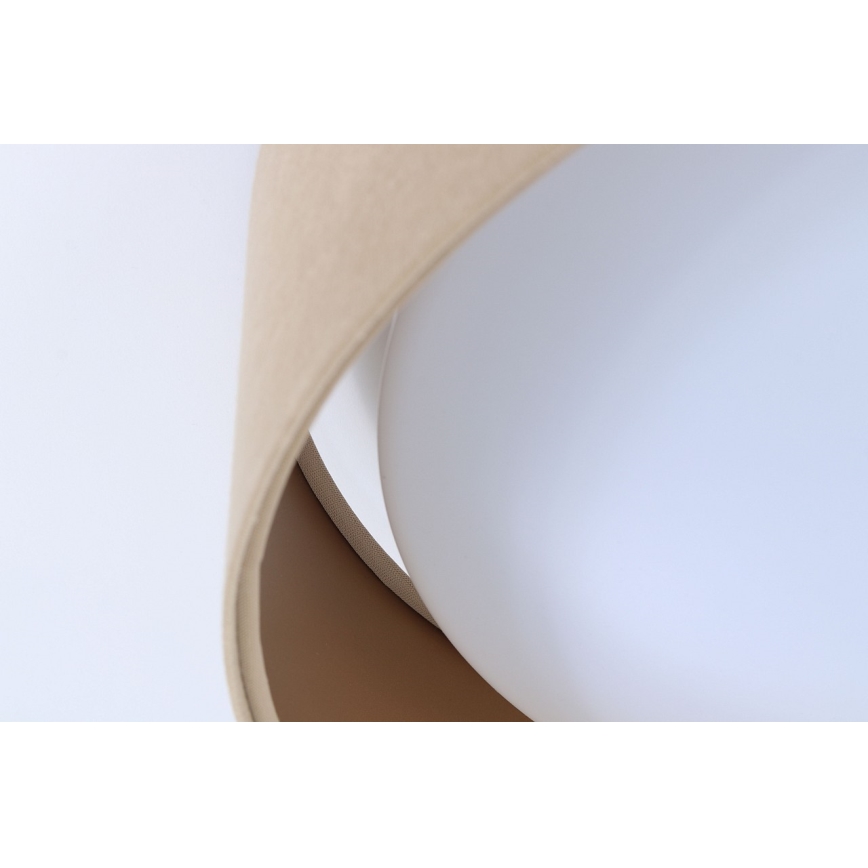 Svietidlo svieti. Je zložené z dvoch častí, svetlejšej a tmavšej béžovej, ktoré obklopujú bielu guľovú časť. Svietidlo je umiestnené na svetlom pozadí.