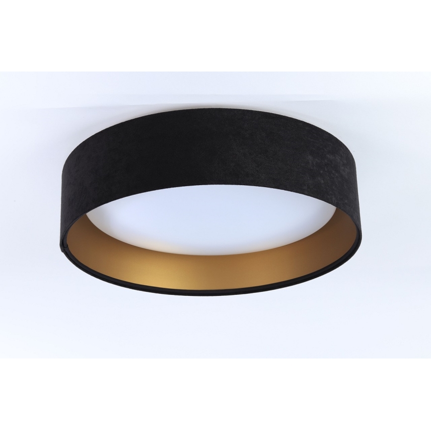 Svietidlo svieti na strope. Je kruhové, má čierny zamatový vrchný diel a zlatý spodný okraj. Strop je biely.