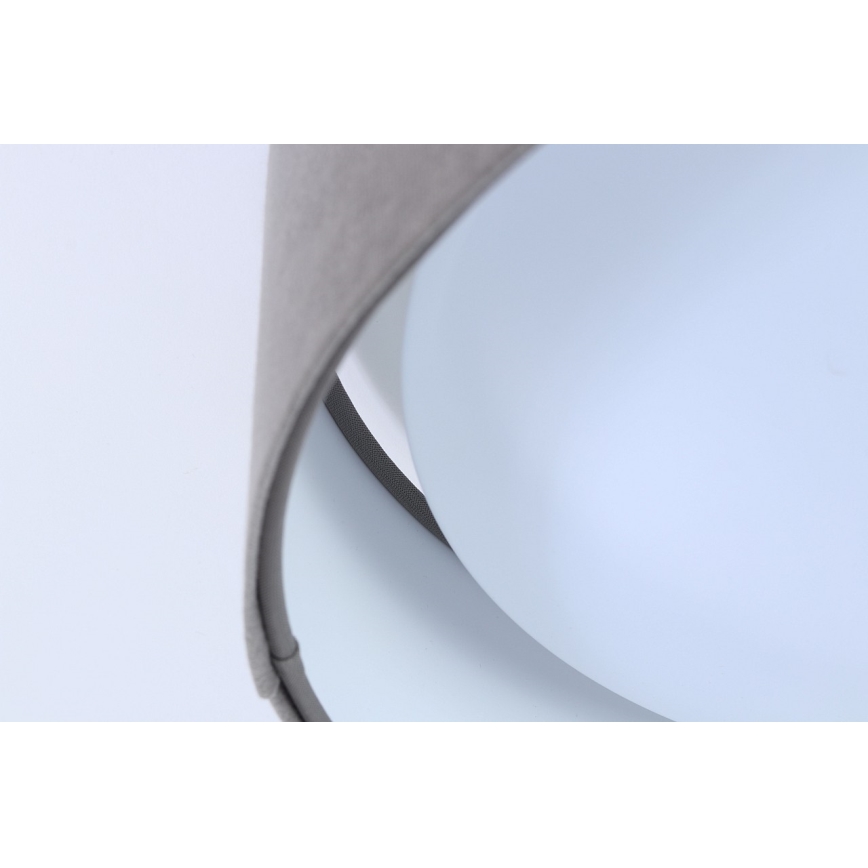 Svietidlo s šedým textilným tienidlom obopínajúce svetlomodrý difúzor. Tienidlo je čiastočne prehnuté. Svetlo je zavesené na bielom pozadí.