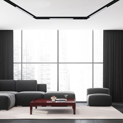 Sivá rohová sedačka stojí v modernej miestnosti pred tmavočerveným konferenčným stolíkom. Miestnosť má veľké okná s výhľadom na mesto a tmavé závesy.