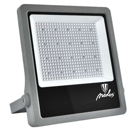 LED reflektor svieti. Je sivý, obdĺžnikového tvaru s čiernym panelom, na ktorom je logo Medes. Má nastaviteľný stojan.