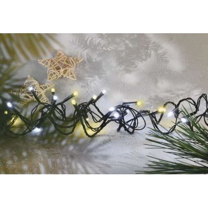 Svetelná reťaz s bielymi a žltými LED diódami leží na svetlom povrchu. Súčasťou scény sú dve slamené hviezdy a vetvička ihličnatého stromu.