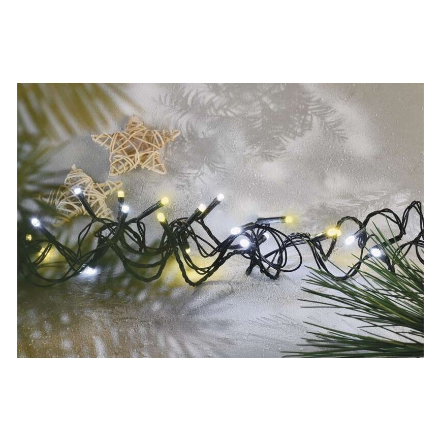 Svetelná reťaz s bielymi a žltými LED diódami leží na svetlom povrchu. Súčasťou scény sú dve slamené hviezdy a vetvička ihličnatého stromu.