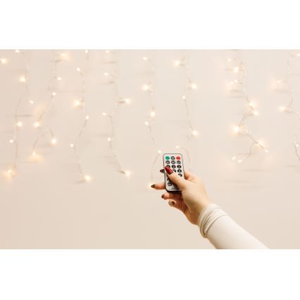 Ruka drží diaľkové ovládanie svetiel. Ovláda svetelnú girlandu s mnohými malými žiarovkami na svetlom pozadí.