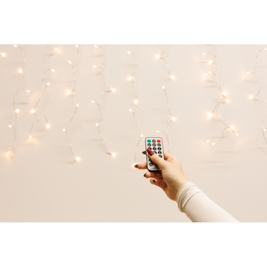 Ruka drží diaľkové ovládanie svetiel. Ovláda svetelnú girlandu s mnohými malými žiarovkami na svetlom pozadí.