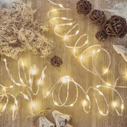 Svetlený LED pásik leží na drevenom povrchu. Okolo sú rozmiestnené malé drevené gule a chumáč svetlohnedého materiálu.