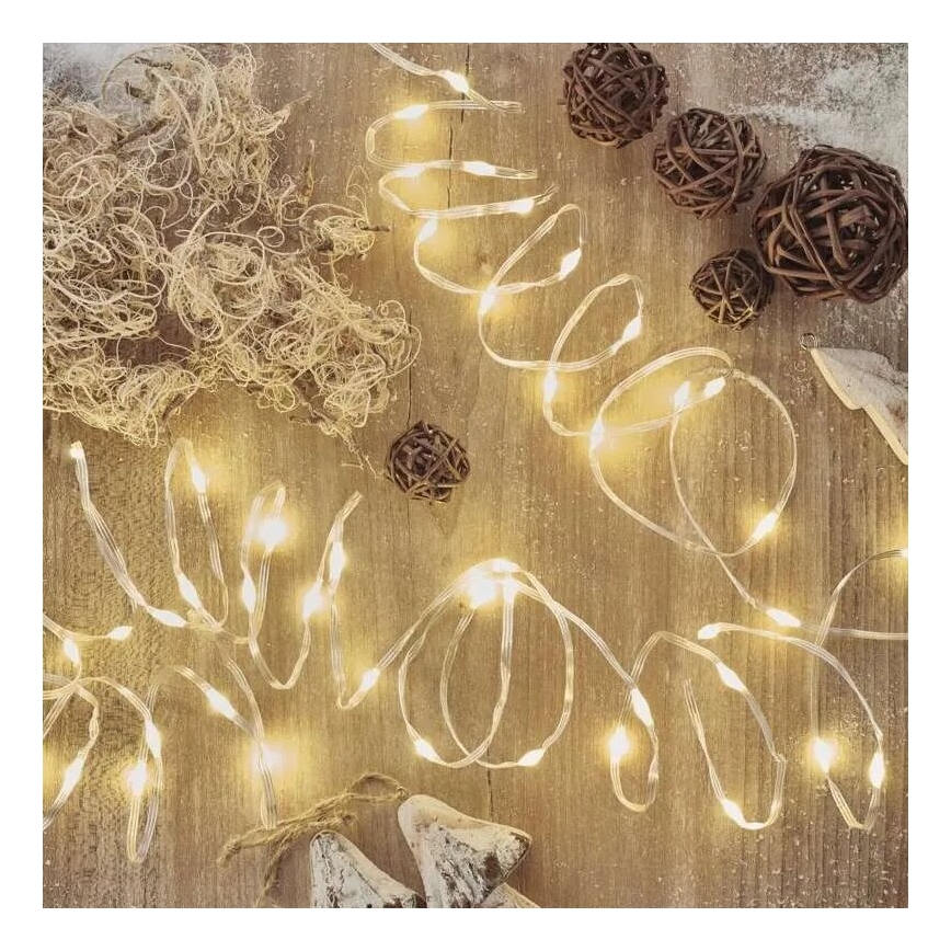 Svetlený LED pásik leží na drevenom povrchu. Okolo sú rozmiestnené malé drevené gule a chumáč svetlohnedého materiálu.