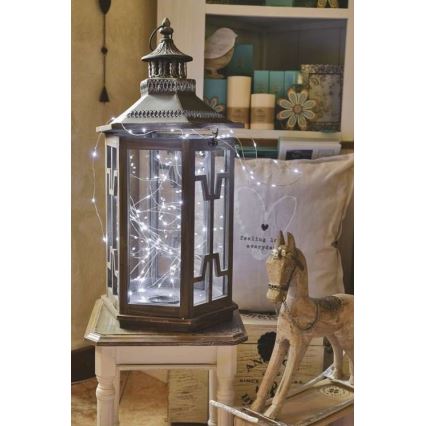 Lampáš s LED svetielkami je umiestený na bielom stolíku. Svetielka sú rozprestreté okolo lampáša a siahajú k hojdaciemu koníkovi s nápisom feeling love everyday na vankúši vedľa neho.