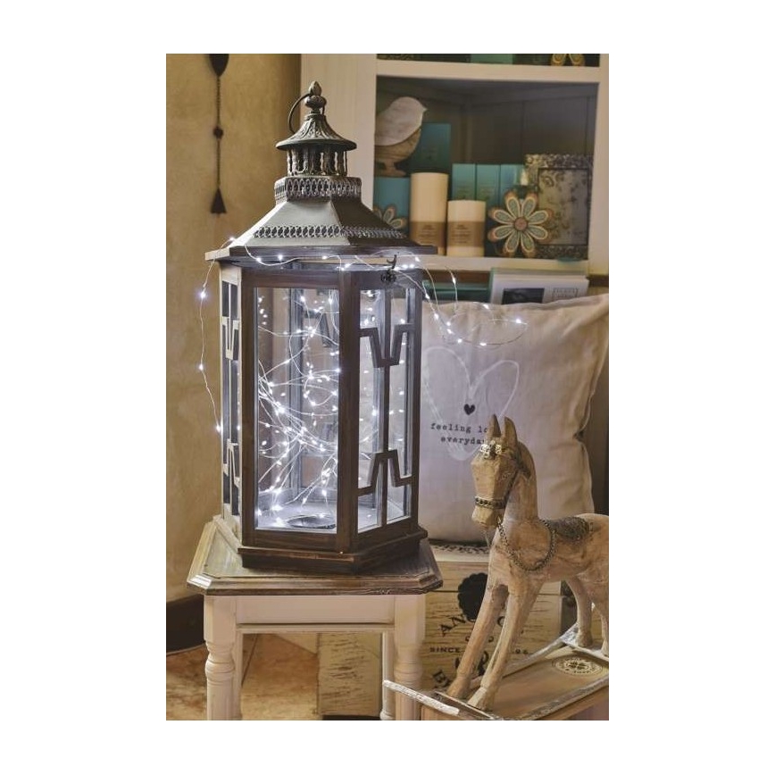 Lampáš s LED svetielkami je umiestený na bielom stolíku. Svetielka sú rozprestreté okolo lampáša a siahajú k hojdaciemu koníkovi s nápisom feeling love everyday na vankúši vedľa neho.