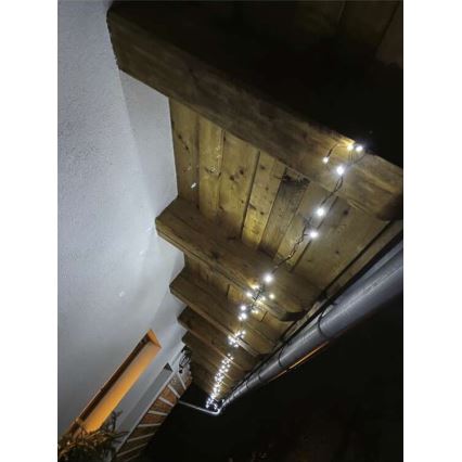 Elektrický svetelný veniec s malými bielymi LED diódami je pripevnený pod dreveným stropom a vedie pozdĺž odkvapového žľabu. Svetlá svietia v nočnom prostredí.