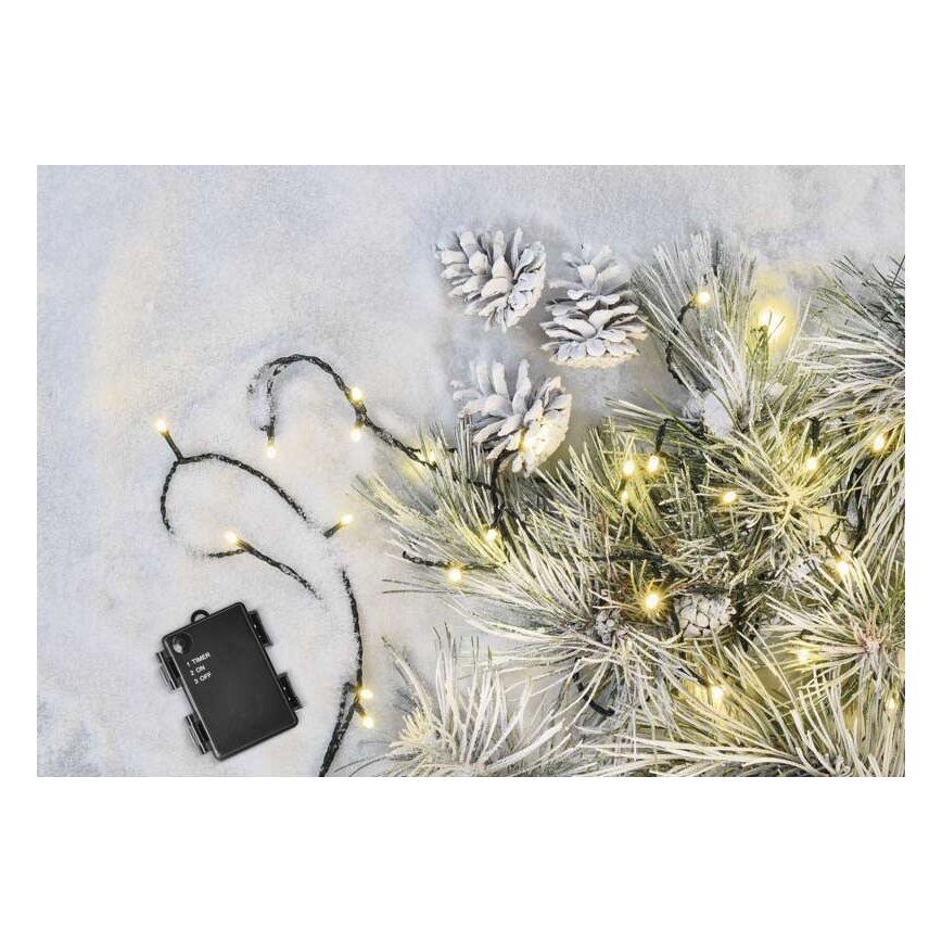 Svetelný veniec s teplými bielymi LED diódami je rozložený na snehu a umiestnený na umelom ihličnane. Pripojená je čierna batéria s popisom: 1. Timer, 2. On, 3. Off.