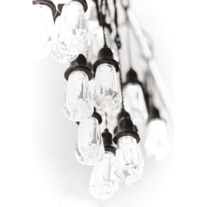 Svietidlo s mnohými visiacimi žiarovkami s čírym sklom a tmavosivými kovovými objímkami. Žiarovky sú zavesené na tenkých kábloch a vytvárajú kaskádu. Svetlé pozadie.