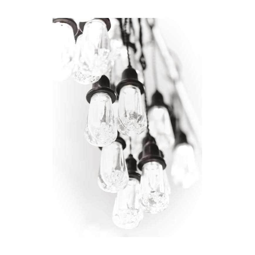 Svietidlo s mnohými visiacimi žiarovkami s čírym sklom a tmavosivými kovovými objímkami. Žiarovky sú zavesené na tenkých kábloch a vytvárajú kaskádu. Svetlé pozadie.