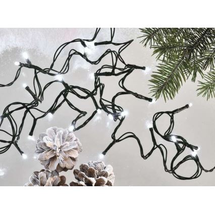 Svetelný reťaz s bielymi LED diódami na čiernom kábli je rozložený na svetlom pozadí. Okolité prvky tvoria šišky a vetvičky ihličnatého stromu.