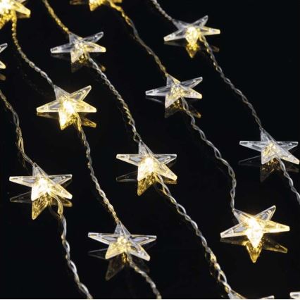 Svetielkujúce hviezdičky v tvare päťcípych hviezd sú pripevnené na tenkých drôtoch, ktoré visia paralelne. Svetlá sú teplej farby a tvoria dekoráciu na tmavom pozadí.