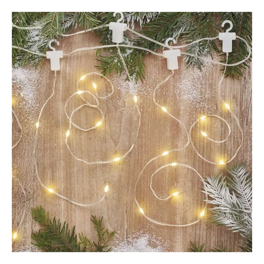 Svetlený elektrický veniec s malými žiarovkami je umiestnený v špirálových závitoch na drevenom povrchu. Veniec je pripevnený k povrchu bielymi sponkami. V okolí sú roztrúsené vetvičky ihličnatého stromu a umelý sneh.