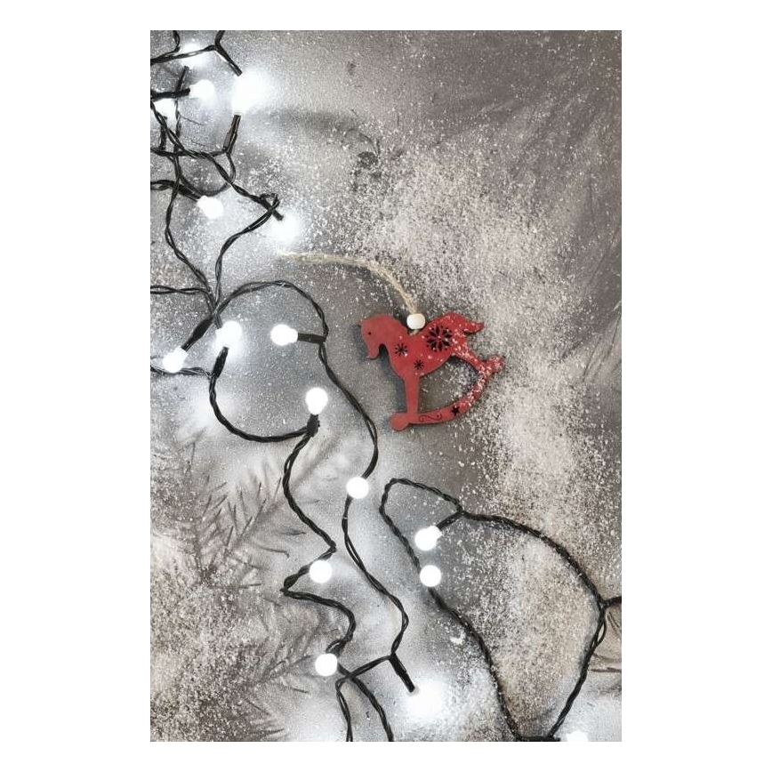 Drevená červená hojdacia kolíska visí na šnúre svetielok. Svetielka sú biele a rozložené na sivom podklade posypanom umelým snehom. V pozadí sú naznačené ihličie.