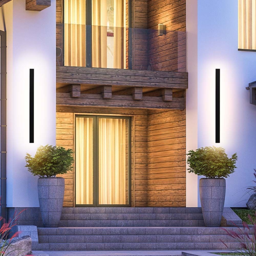 Dve vysoké, úzke, čierne vonkajšie svietidlá svietia pri vchode do domu. Dom má drevený obklad a kamenné schody. Pri každom svietidle je vysadený ker v kameninovom kvetináči.