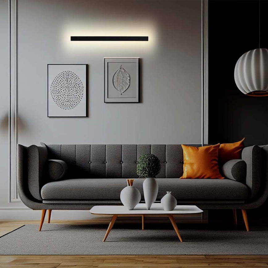 Dlhá čierna LED lampa svieti na stene obývačky. Pred ňou je šedá sedačka s oranžovými vankúšmi a konferenčný stolík s vázy. Na stene sú dva obrazy.