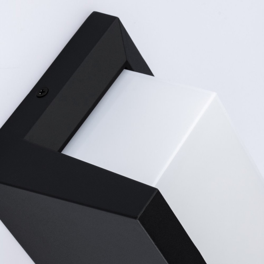 Čierno-biela nástenná lampa s hranatým dizajnom je pripevnená na stene. Lampa je umiestnená v pravom hornom rohu. Viditeľné je pripojenie kábla.