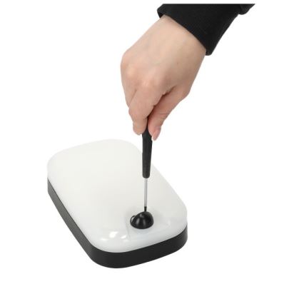 Ruka drží skrutkovač a otáča ním malý čierny diel na obdĺžnikovom bielom svietidle s čiernym rámom. Svietidlo leží na bielom pozadí.