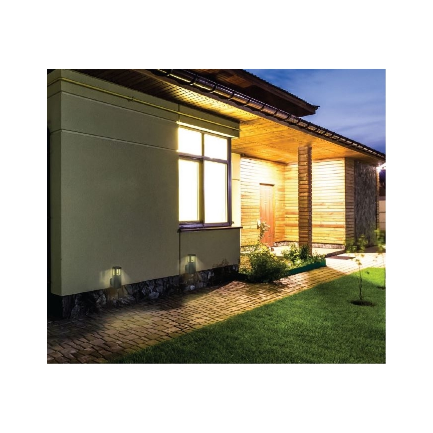 Dve vonkajšie nástenné svietidlá osvetľujú chodník pred domom. Svietidlá sú umiestnené na vonkajšej stene domu v noci. Dom má drevené obloženie a osvetlené okno.