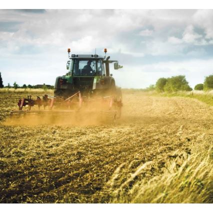 Traktor orie orá pole. Za ním sa dvíha prach. Poľnohospodárska krajina s nízkou vegetáciou.