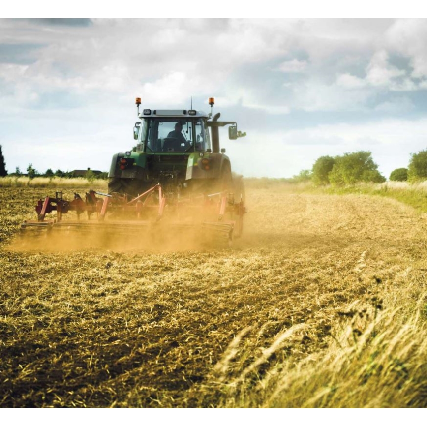 Traktor orie orá pole. Za ním sa dvíha prach. Poľnohospodárska krajina s nízkou vegetáciou.