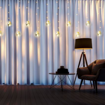 Svetlá vo forme guličiek visia na závesoch. V miestnosti je umiestnený kreslo a stolík. Na stolíku sú knihy a šálka. V pozadí stojí stojacia lampa.