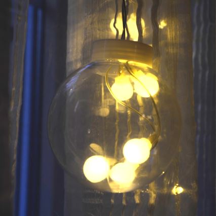 Sklenená guľa s vnútorným osvetlením zo žiaroviek visí na závesoch. Svetlo zo žiaroviek presvitá cez sklo.