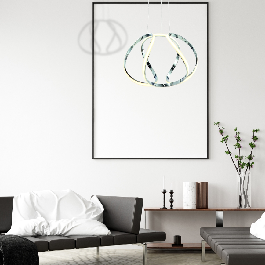 Závesné svietidlo svieti. Je z chrómovanej ocele, pozostáva z prepletených kruhov s LED osvetlením. Svietidlo je zavesené zo stropu na kábloch.