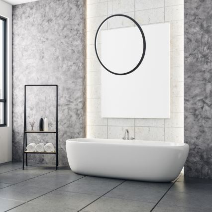 Vanková vaňa stojí v modernej kúpeľni s betónovou stenou a dlaždicovou podlahou. Vedľa nej je stojan s uterákmi a kozmetikou. Nad vaňou visí veľká biela plocha s okrúhlym prvkom.