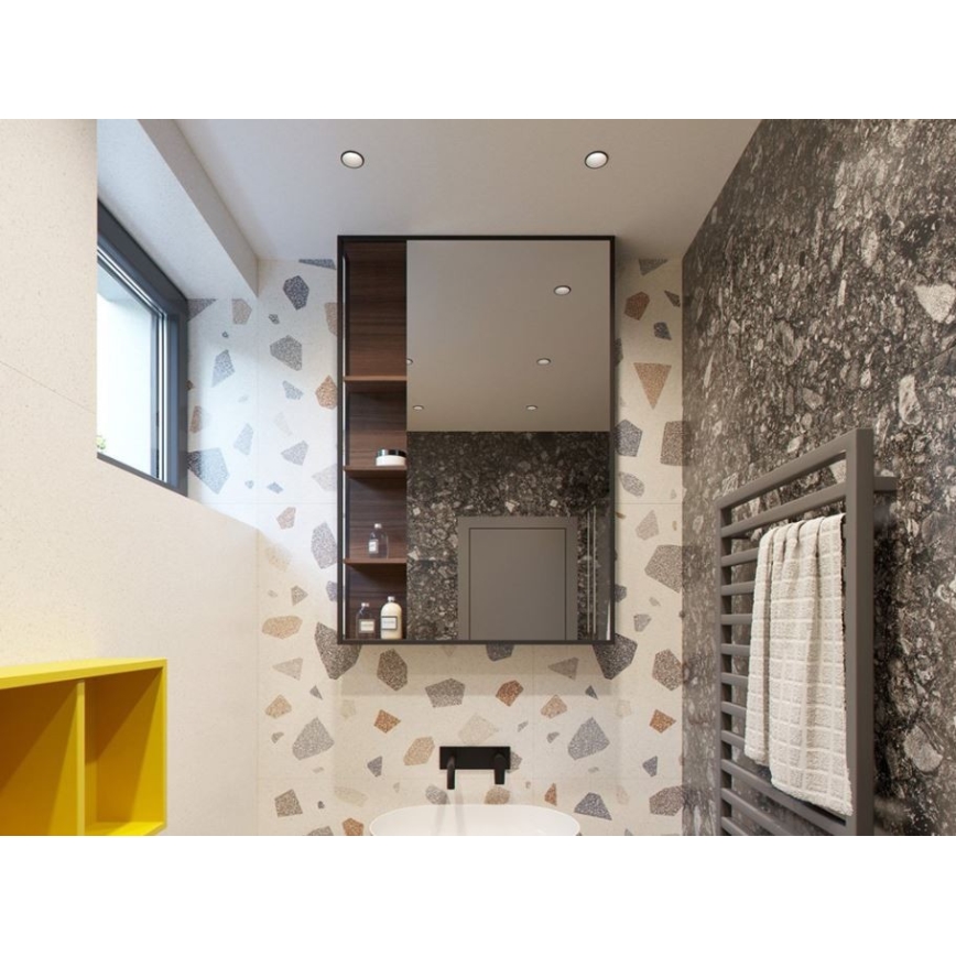 Zrkadlo s poličkami odráža kúpeľňu s dlažbou z mramoru a farebnými kamienkami. Kúpeľňa obsahuje žltú skrinku, radiátor s uterákom a umývadlo.