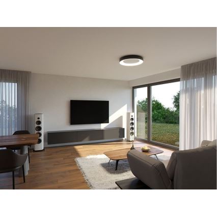 Reproduktory stoja v obývacej izbe s drevenou podlahou, televízorom na stene a sedačkou. Okná vedú do záhrady.