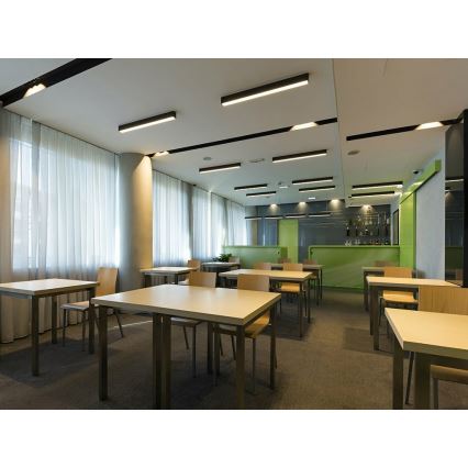 Stôl stojí v miestnosti s viacerými stolmi a stoličkami, v pozadí je bar. Miestnosť je moderne zariadená, má koberec a veľké okná so závesmi. Na strope sú umiestnené lineárne svietidlá.