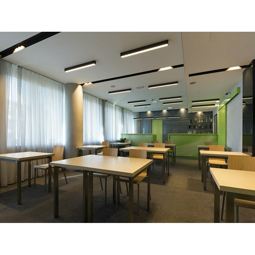 Stôl stojí v miestnosti s viacerými stolmi a stoličkami, v pozadí je bar. Miestnosť je moderne zariadená, má koberec a veľké okná so závesmi. Na strope sú umiestnené lineárne svietidlá.