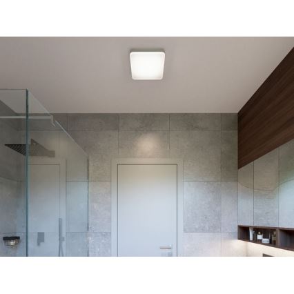 Štvorcové svietidlo je osvetlené na strope. Nachádza sa v kúpeľni s dlaždicami a sprchovým kútom. V pozadí je dvere.