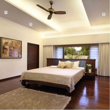 Veľká posteľ stojí v spálni s drevenou podlahou. Na strope je stropný ventilátor a zabudované svetlá. Okná sú zavesené závesmi.