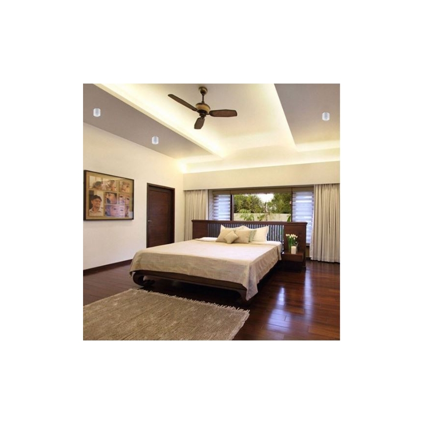 Veľká posteľ stojí v spálni s drevenou podlahou. Na strope je stropný ventilátor a zabudované svetlá. Okná sú zavesené závesmi.