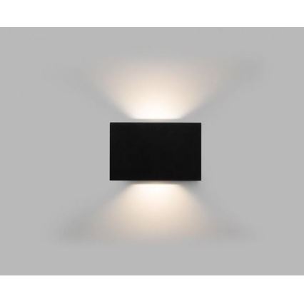 Nástená lampa svieti. Čierna obdĺžniková lampa je pripevnená na svetlej stene. Svetlo svieti oboma smermi.