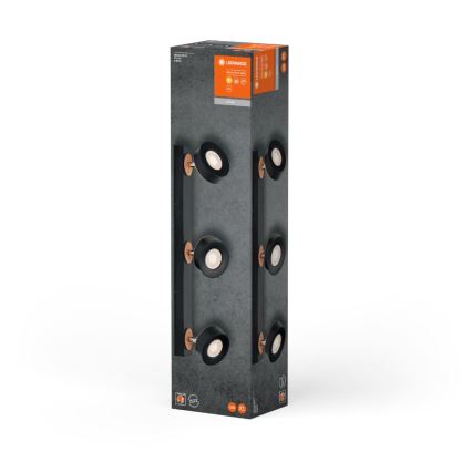 Balenie s nástenným svietidlom: Čierny, štvorbodový reflektor s medenými detailmi je zobrazený na obale. Svietidlo je umiestnené na vertikálne orientovanej krabici.