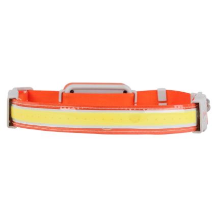 Čelová lampa s oranžovým popruhom a svetlo žltým LED pásikom svieti. Lampa je umiestnená na bielom pozadí.
